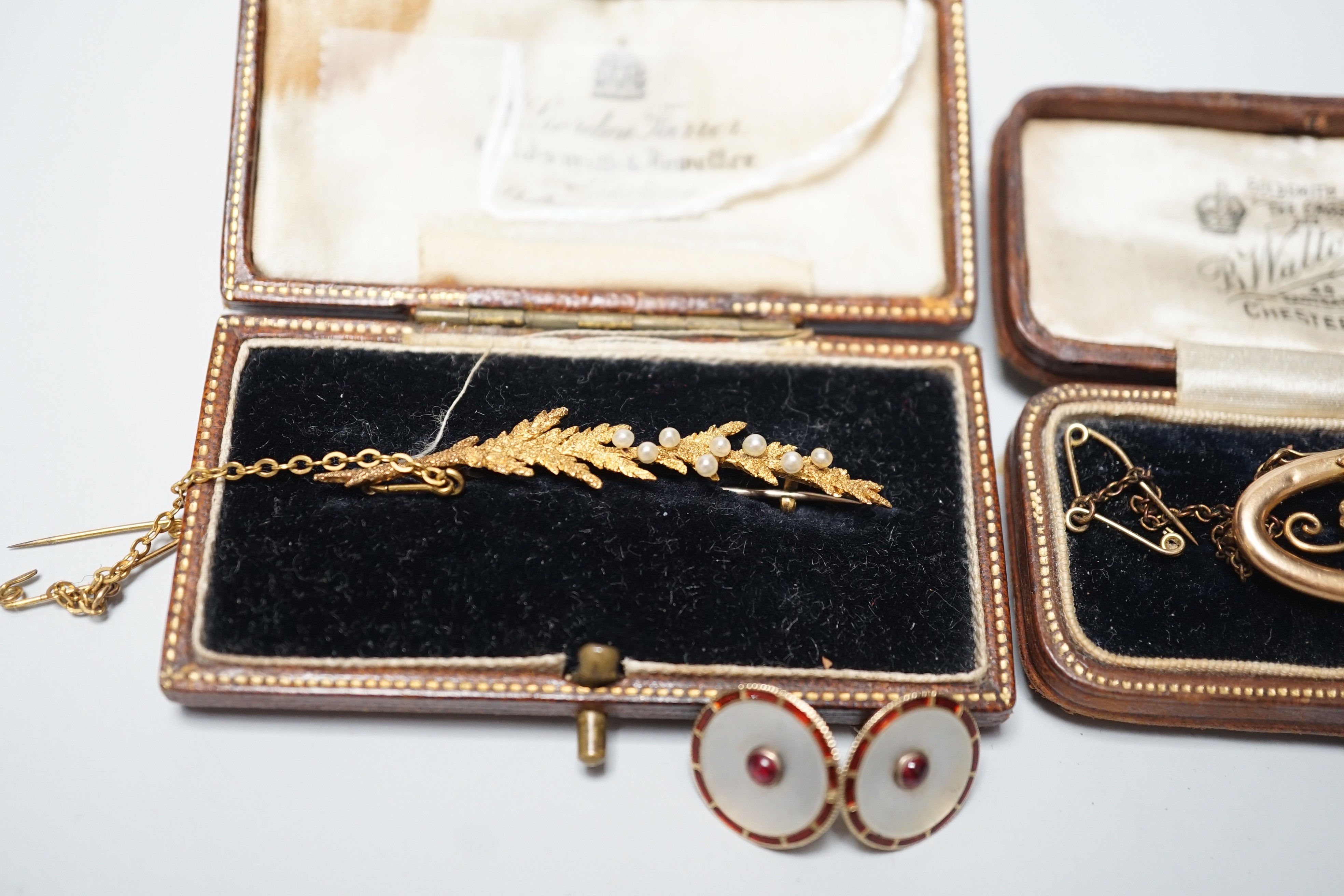 An early 20th century 15ct and seed pearl set leaf brooch, 51mm, one other 15ct and seed pearl brooch and a pair of 15ct, enamelled and gem set ear studs (converted buttons), gross weight 10 grams.